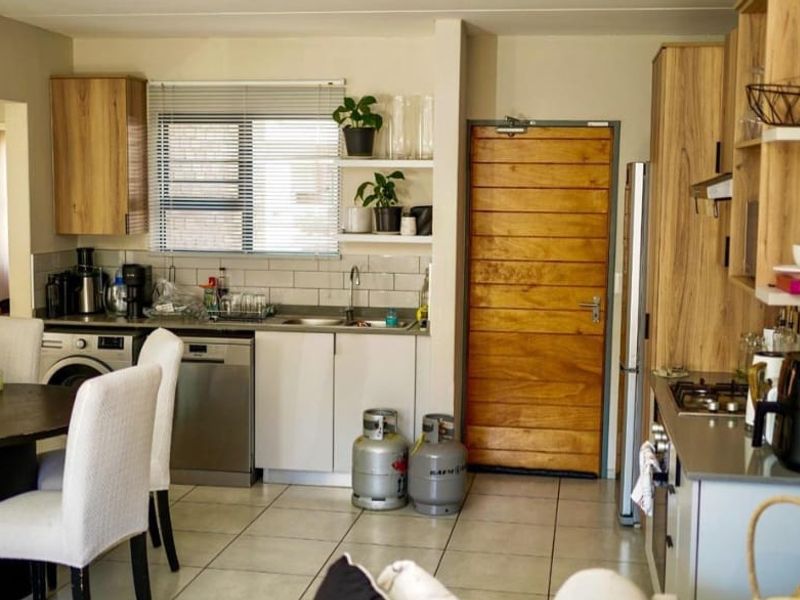 Open-plan kitchen and dining area featuring modern cabinetry, subway tile backsplash, gas hob, and tiled flooring with direct access to an exterior door.