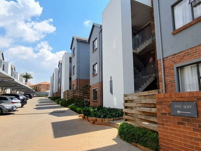 Exterior view of a modern apartment complex featuring brick and rendered facades, covered parking bays, and paved access paths.