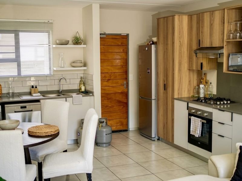 Modern open-plan kitchen featuring wood-look cabinetry, gas hob, electric oven, and tiled flooring, seamlessly integrated with the dining and living area.