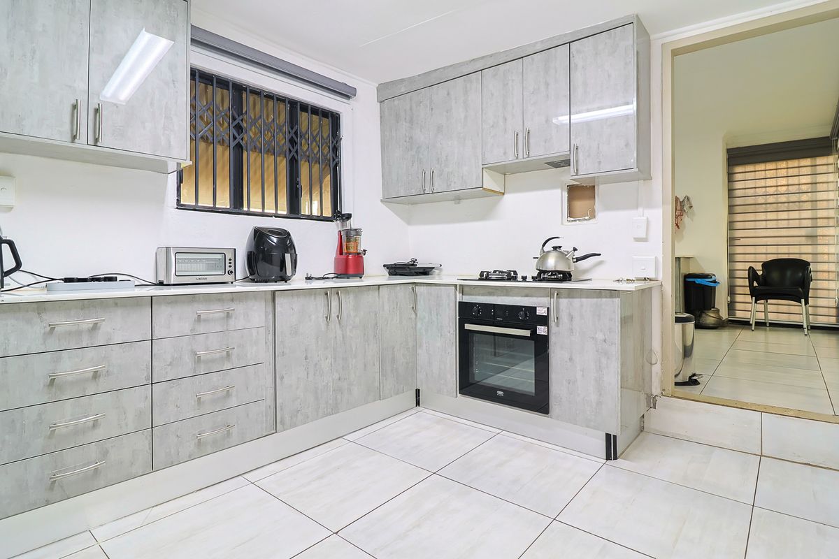 Functional kitchen featuring grey laminate cabinetry, built-in oven, gas hob, and tiled flooring, with a security gate installed on the window.