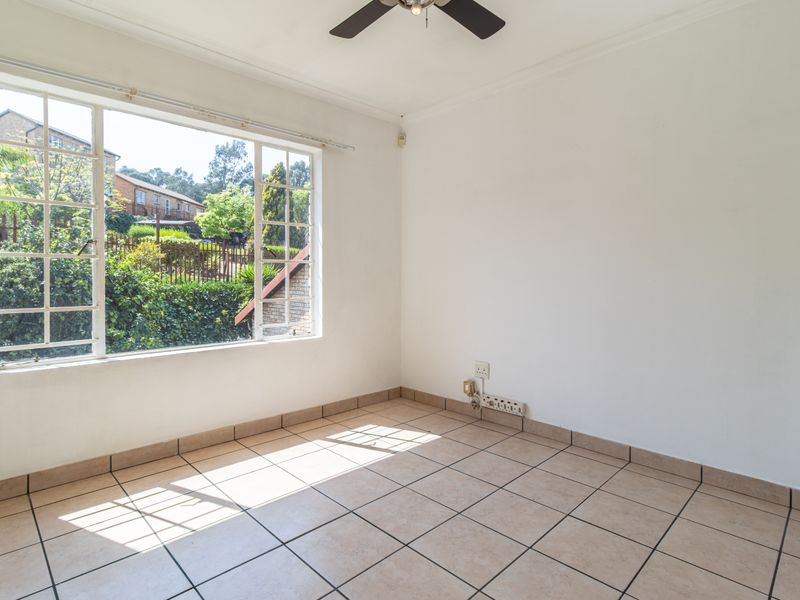 A bright, empty bedroom featuring tiled flooring, a ceiling fan, and a large window providing natural light and a view of the exterior.