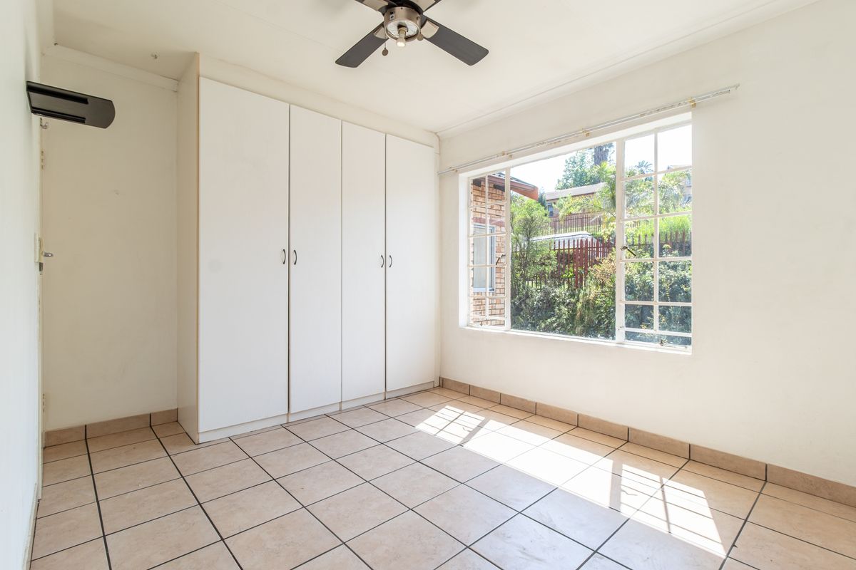 A bright, empty bedroom featuring built-in cupboards, tiled flooring, and a ceiling fan, offering a clean canvas for personalization.