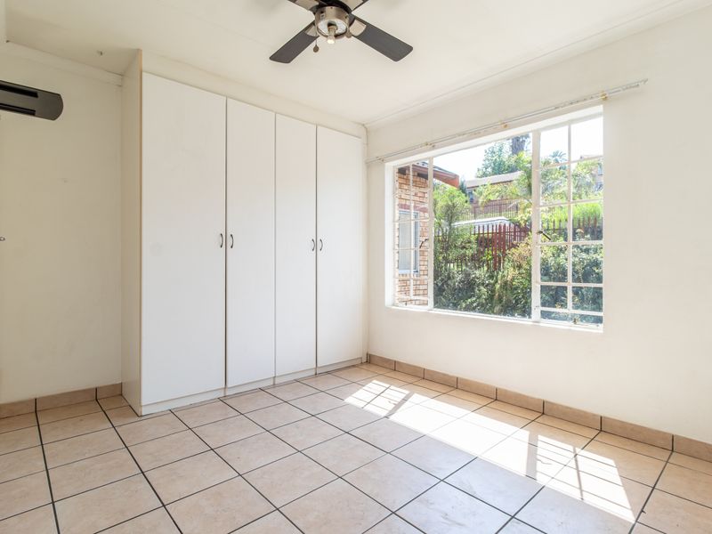 A bright, empty bedroom featuring built-in cupboards, tiled flooring, and a ceiling fan, offering a clean canvas for personalization.