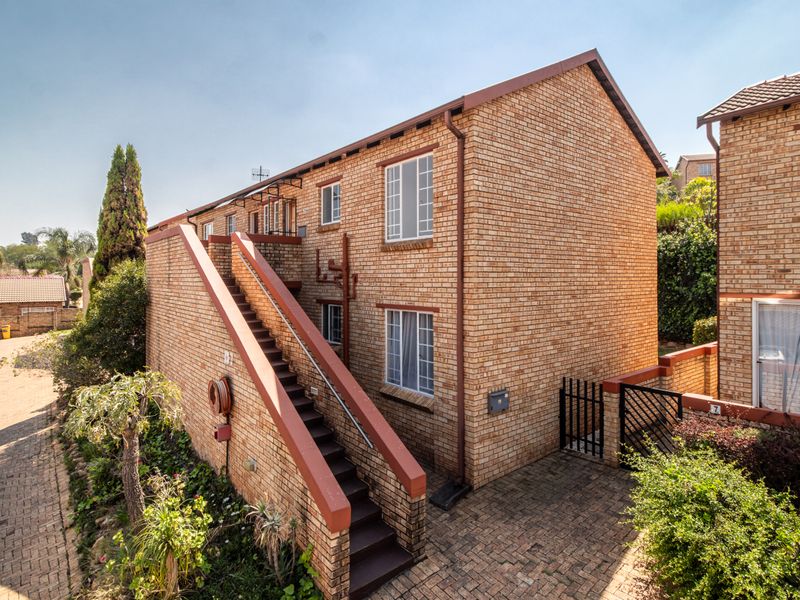 Exterior view of a face brick apartment building featuring an external staircase, paved driveway, and secure gated access.
