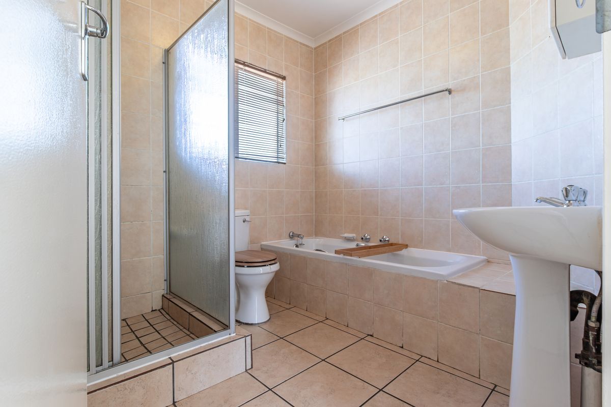 A functional bathroom featuring a shower enclosure, bathtub, pedestal basin, and toilet with neutral wall and floor tiling.