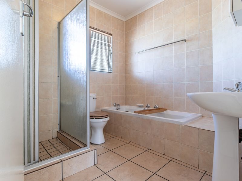 A functional bathroom featuring a shower enclosure, bathtub, pedestal basin, and toilet with neutral wall and floor tiling.