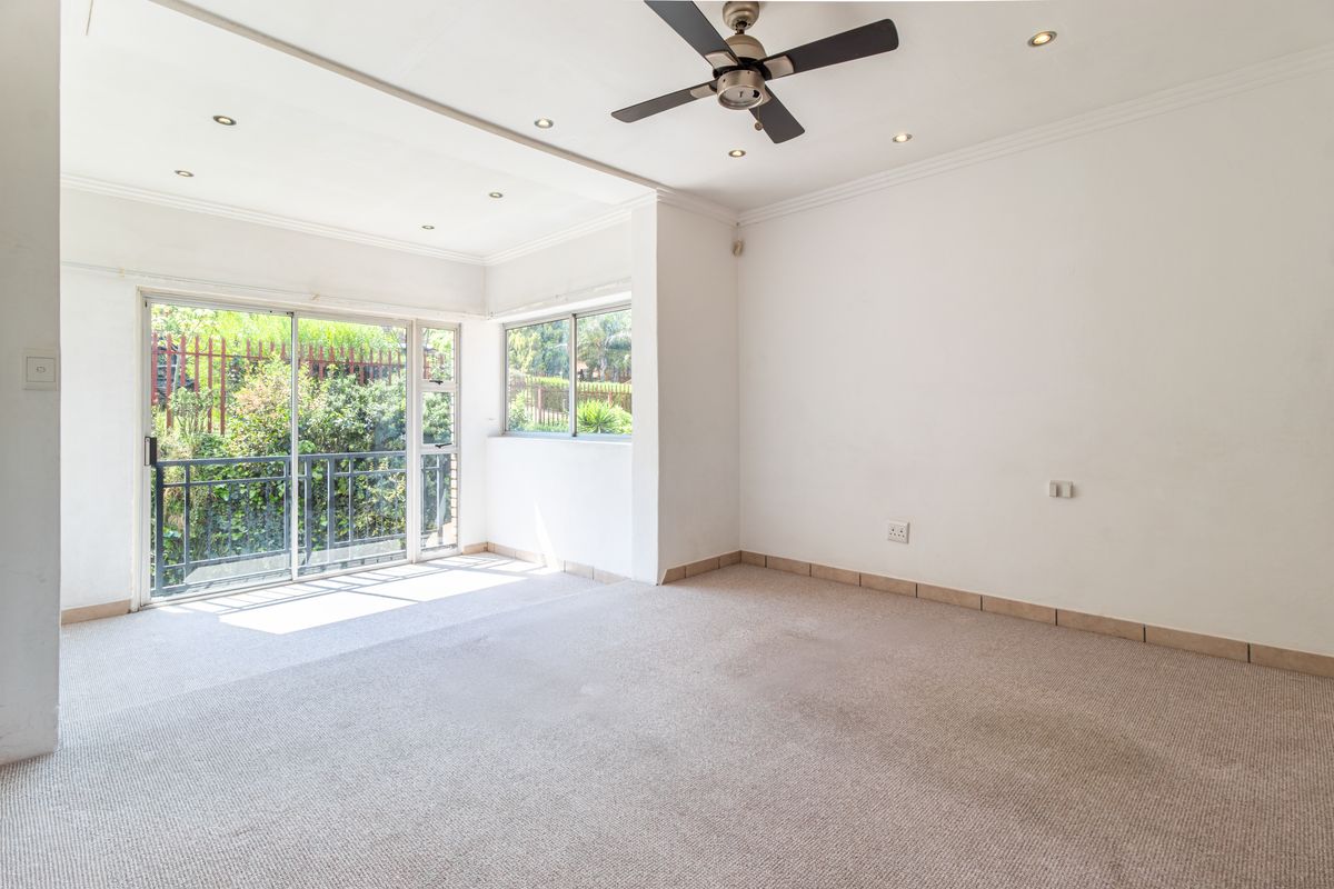 An empty, sunlit living room featuring neutral carpeting, a ceiling fan, recessed lighting, and sliding glass doors leading to an outdoor area.