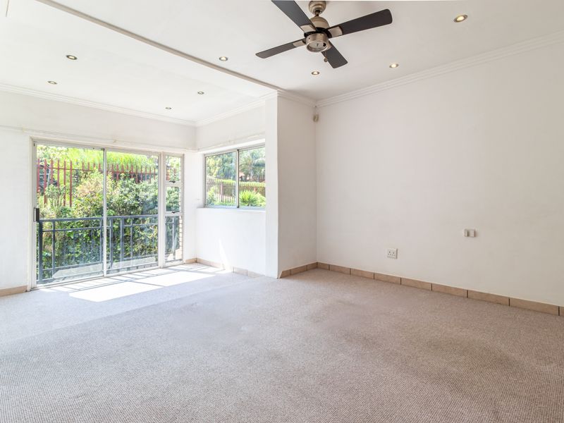 An empty, sunlit living room featuring neutral carpeting, a ceiling fan, recessed lighting, and sliding glass doors leading to an outdoor area.
