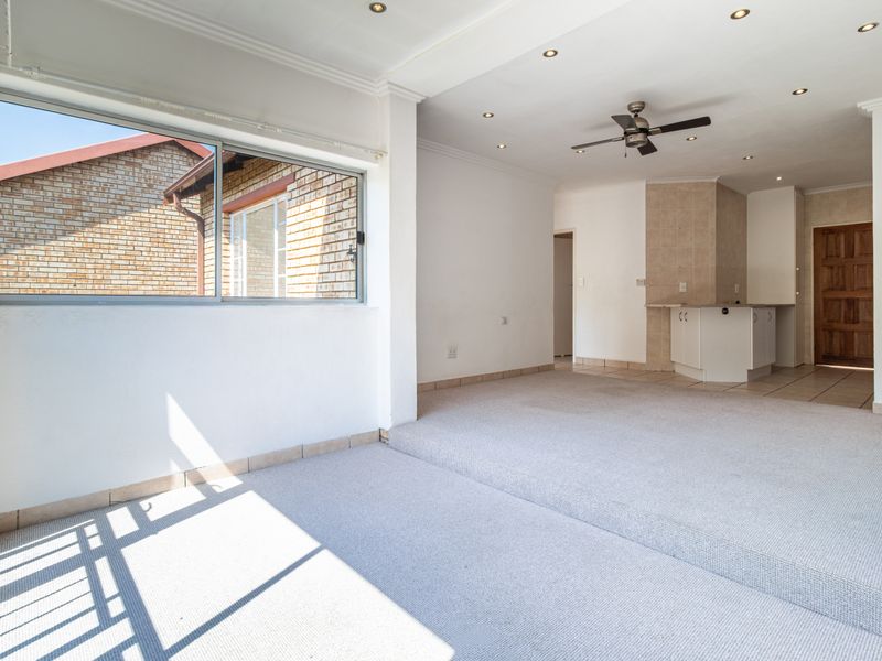 Spacious open-plan living area featuring a raised carpeted section, recessed lighting, ceiling fan, and an adjoining kitchen area with tiled finishes.