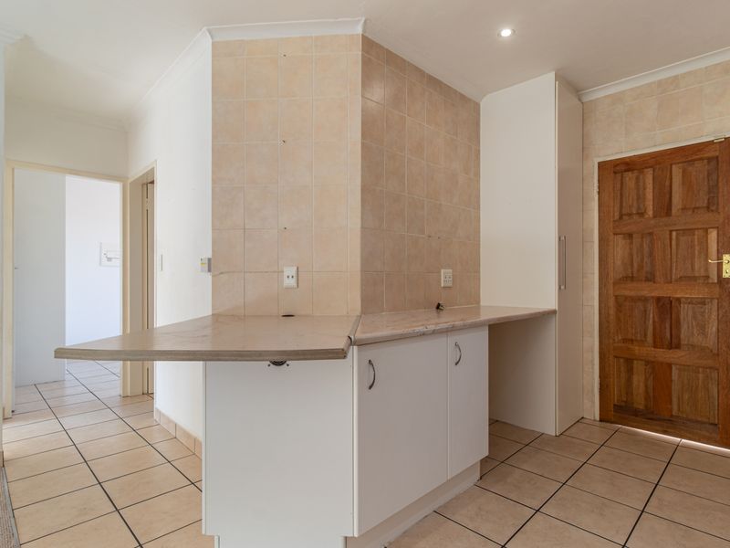 A functional kitchen area featuring tiled flooring, a tiled splashback, laminate countertops, and built-in cabinetry, providing a clean and neutral foundation for updates.