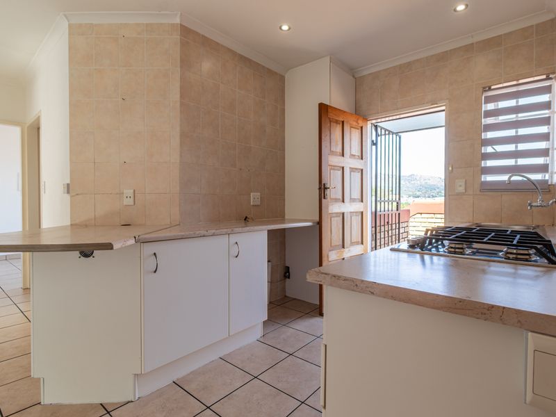 A functional kitchen featuring built-in cabinetry, laminate countertops, a gas hob, and tiled finishes, with direct access to an outdoor area.