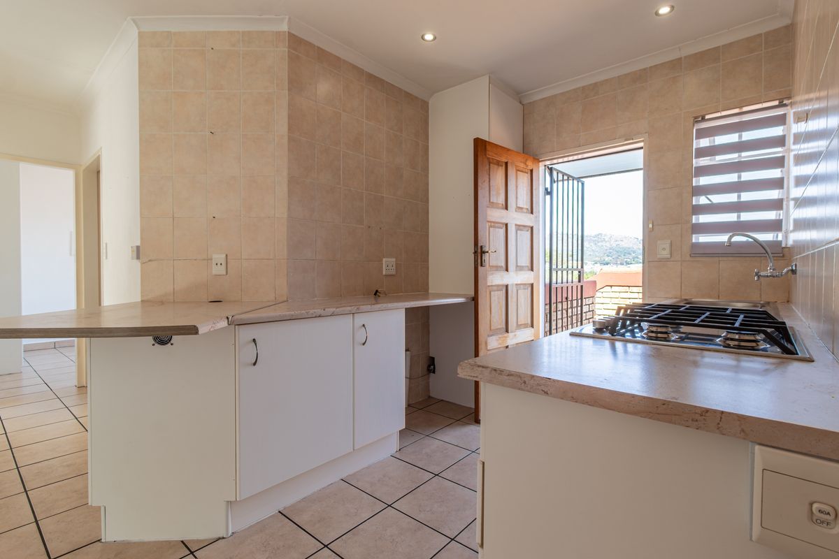 A functional kitchen featuring built-in cabinetry, laminate countertops, a gas hob, and tiled finishes, with direct access to an outdoor area.