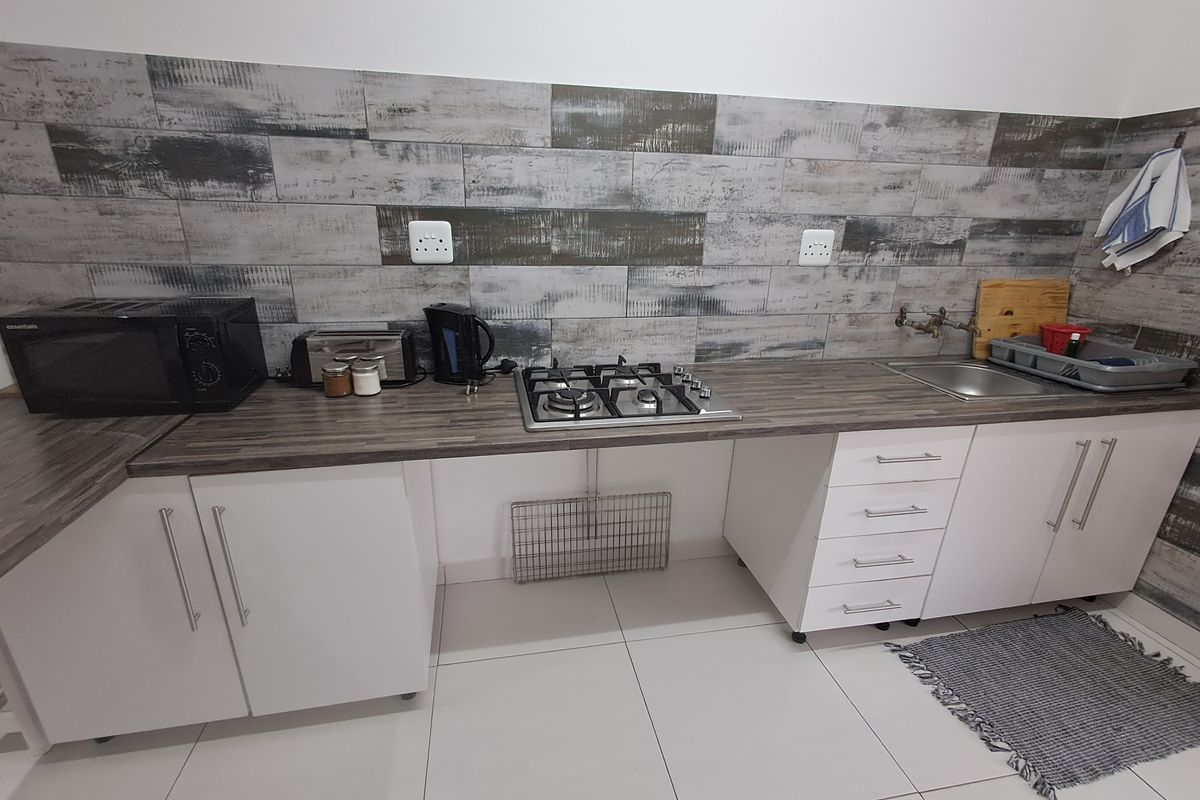 A functional kitchen area featuring a gas hob, laminate countertops, white cabinetry, and a decorative tiled splashback.