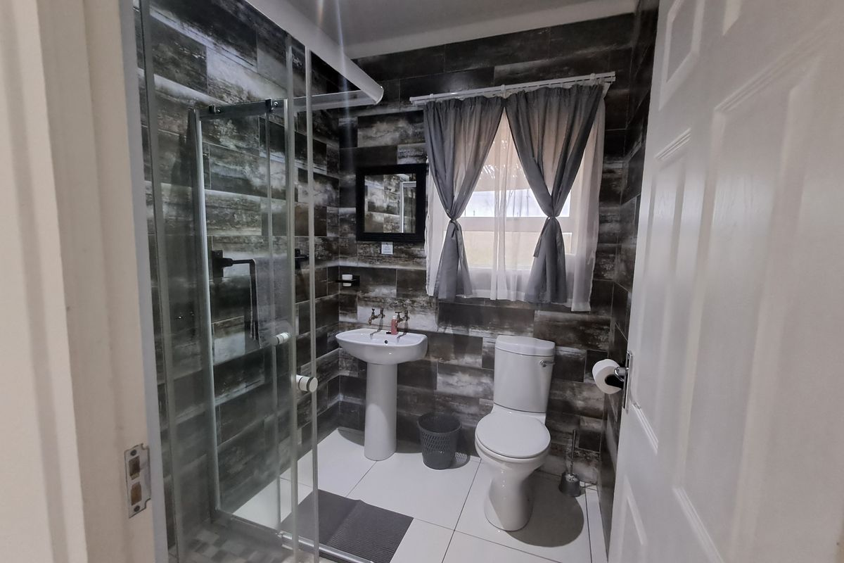 A modern bathroom featuring a glass shower enclosure, pedestal basin, and toilet, finished with dark wood-look wall tiles and white floor tiles.