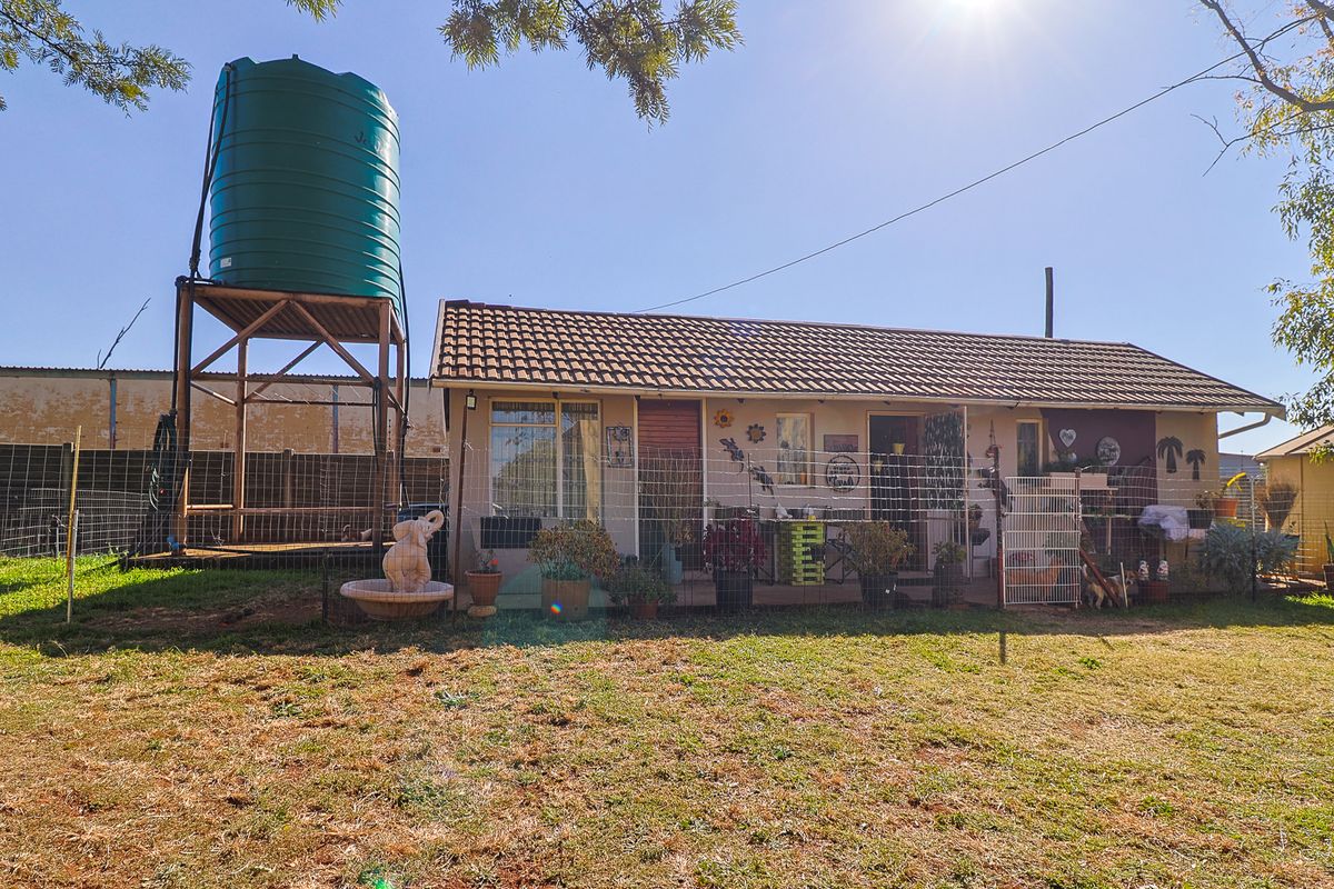 Rear view of the property featuring a covered patio area, a large water storage tank on a stand, and surrounding garden space.