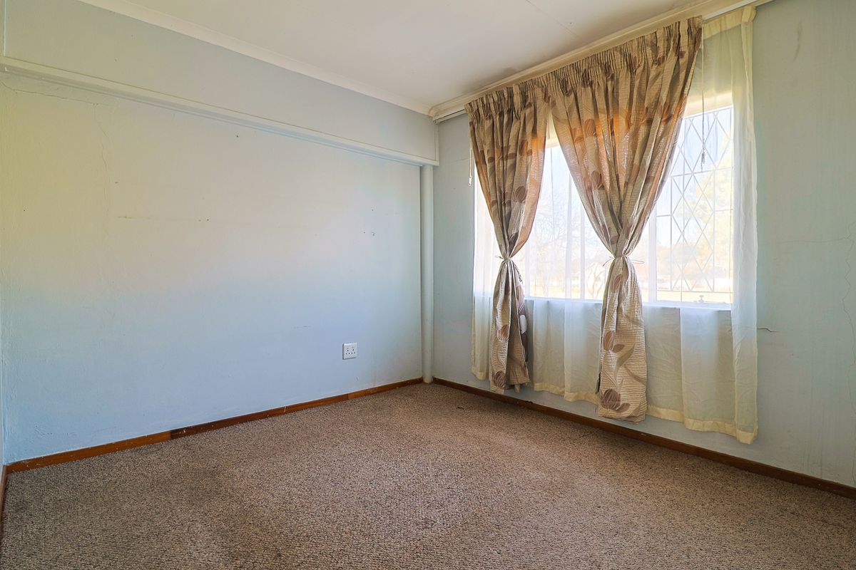 A vacant bedroom featuring carpeted flooring, a window with security bars, and neutral wall finishes, offering a blank canvas for renovation.