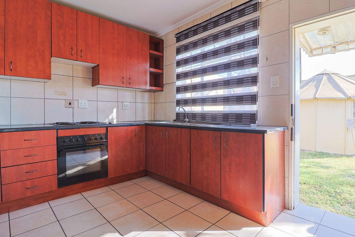 A functional kitchen featuring wood-finish cabinetry, dark laminate countertops, built-in oven and hob, and direct access to the rear garden area.
