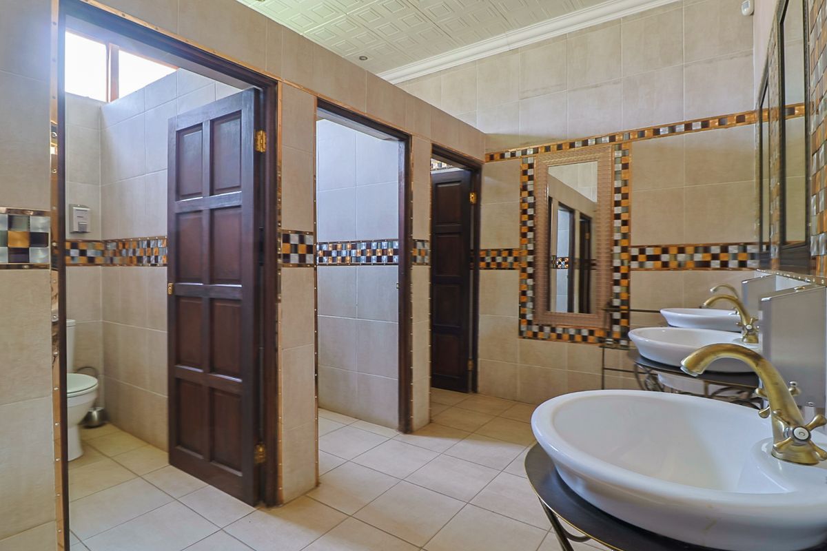 Spacious communal bathroom featuring multiple vanity basins with brass taps, tiled walls with decorative mosaic accents, and private toilet cubicles.