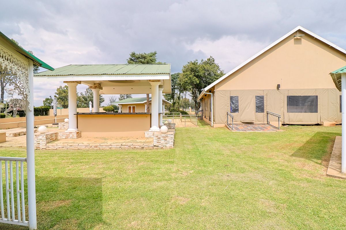 Spacious rear garden area featuring a covered outdoor bar with stone detailing and a building with canvas-enclosed walls and tiled patio access.