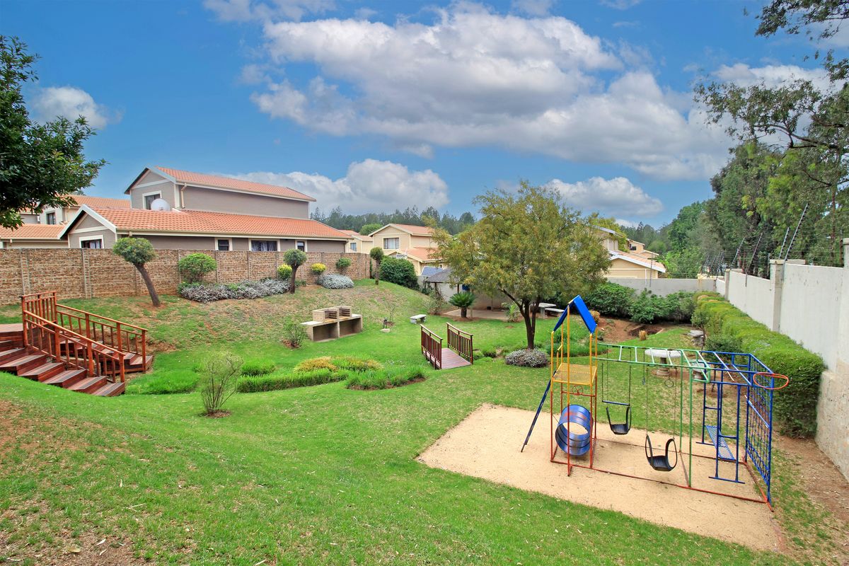 Spacious rear garden featuring a built-in brick braai, wooden decking, a small footbridge, and a dedicated play area within a landscaped setting.