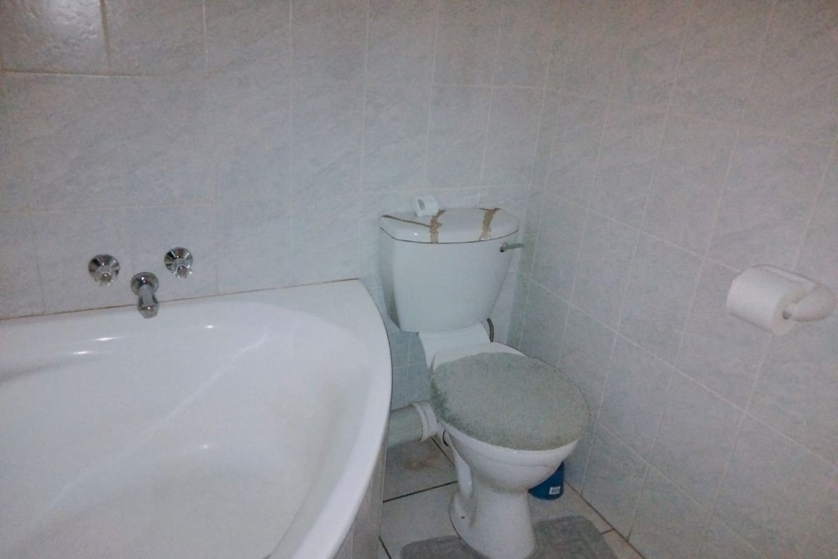 A functional bathroom featuring a built-in bathtub and toilet with full-height wall tiling and tiled flooring.