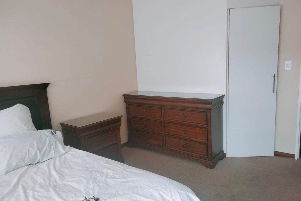 A bedroom featuring neutral wall tones, carpeted flooring, and a built-in cupboard with a modern handle.