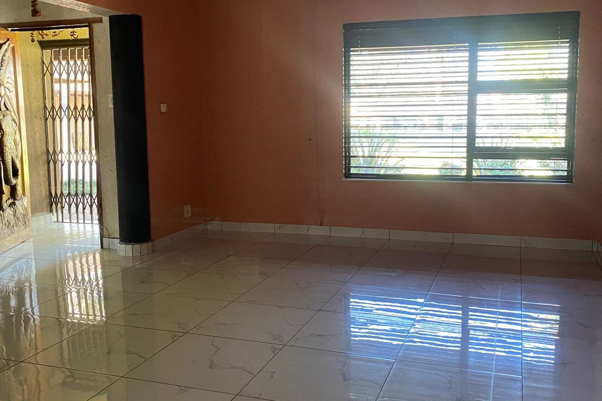 Spacious living area featuring polished marble-look floor tiles, decorative ceiling cornices, and a large window with fitted blinds.