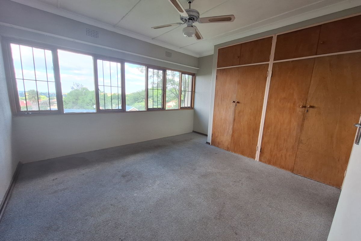 An empty bedroom featuring built-in wooden cupboards, a ceiling fan, and large windows providing natural light and exterior views.