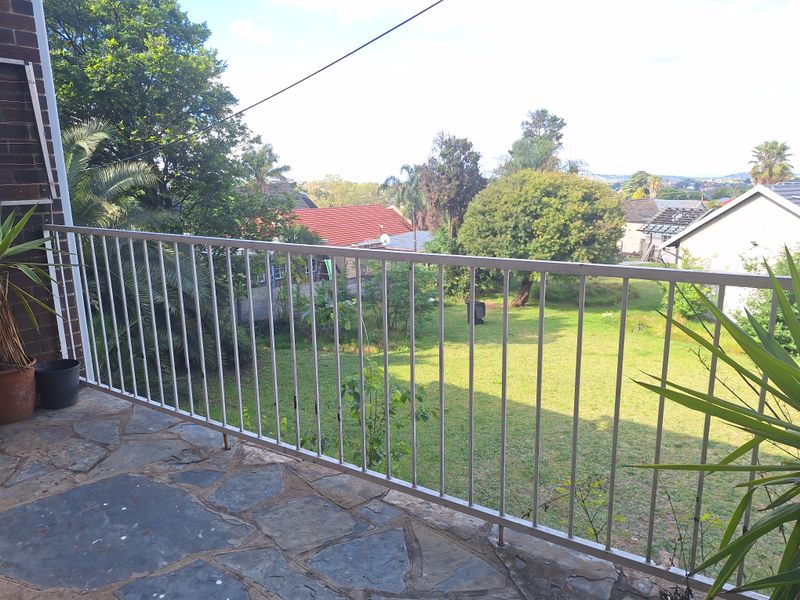 An elevated balcony featuring a metal balustrade and stone crazy paving, overlooking a residential garden area.
