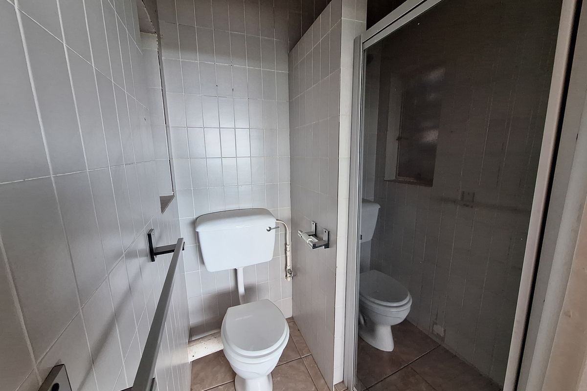 A functional bathroom featuring a toilet and a separate shower enclosure with tiled walls and flooring, presenting an opportunity for modernization.