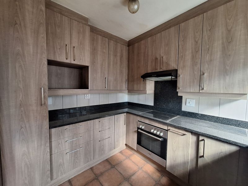 A functional kitchen featuring wood-look laminate cabinetry, granite countertops, and built-in cooking appliances, finished with a tiled backsplash and terracotta flooring.