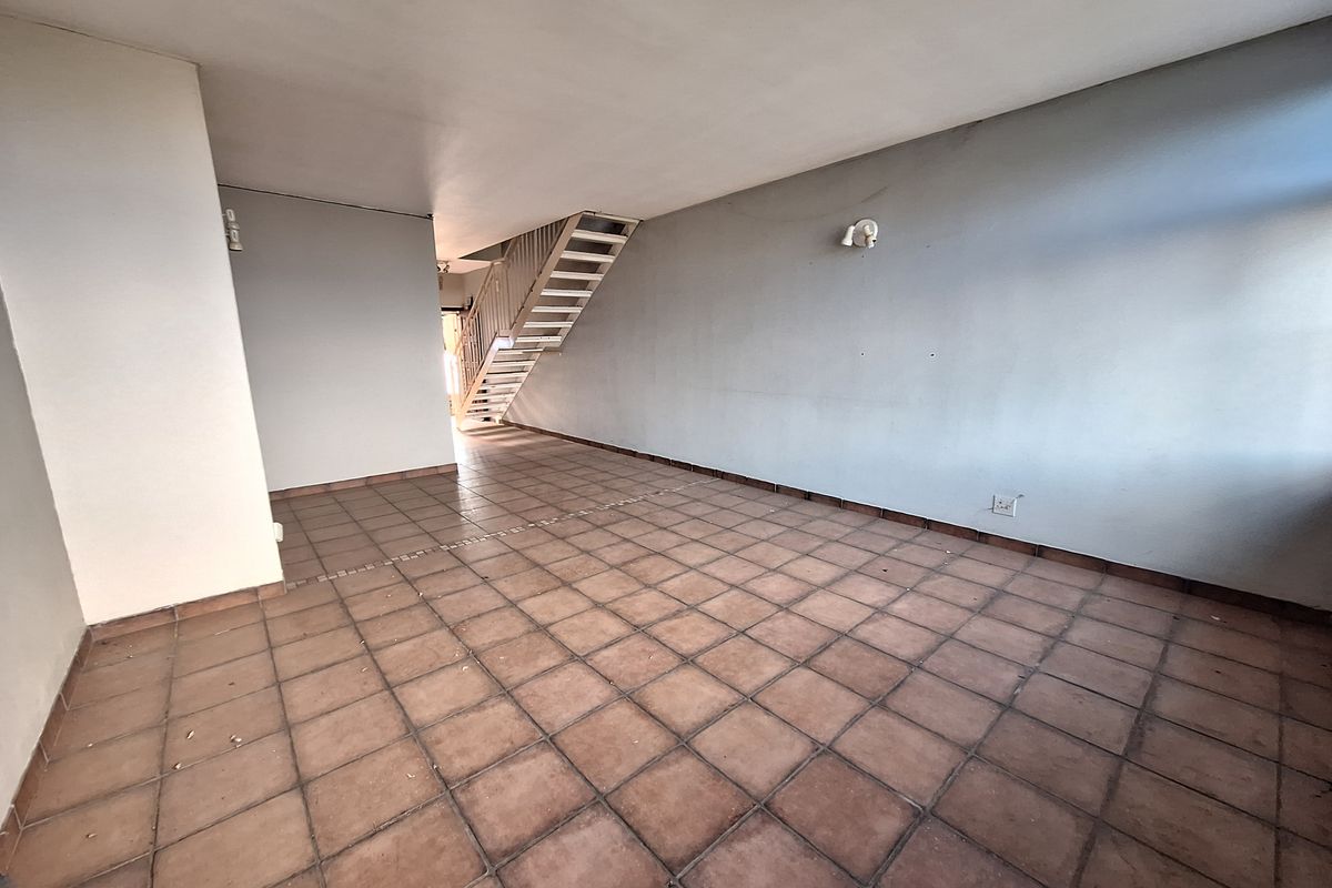 An empty, open-plan living area featuring tiled flooring and a staircase leading to the upper level, offering a blank canvas for renovation.