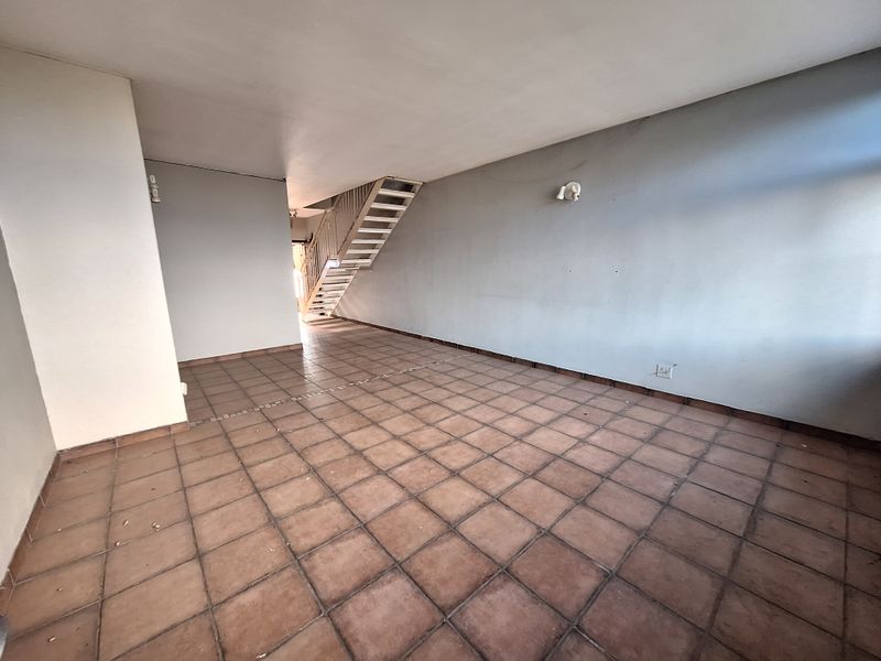 An empty, open-plan living area featuring tiled flooring and a staircase leading to the upper level, offering a blank canvas for renovation.