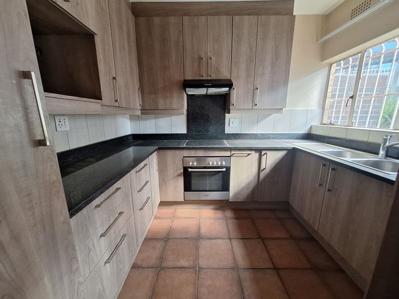 A functional kitchen featuring wood-look laminate cabinetry, granite countertops, built-in oven, electric hob, and a double bowl stainless steel sink.