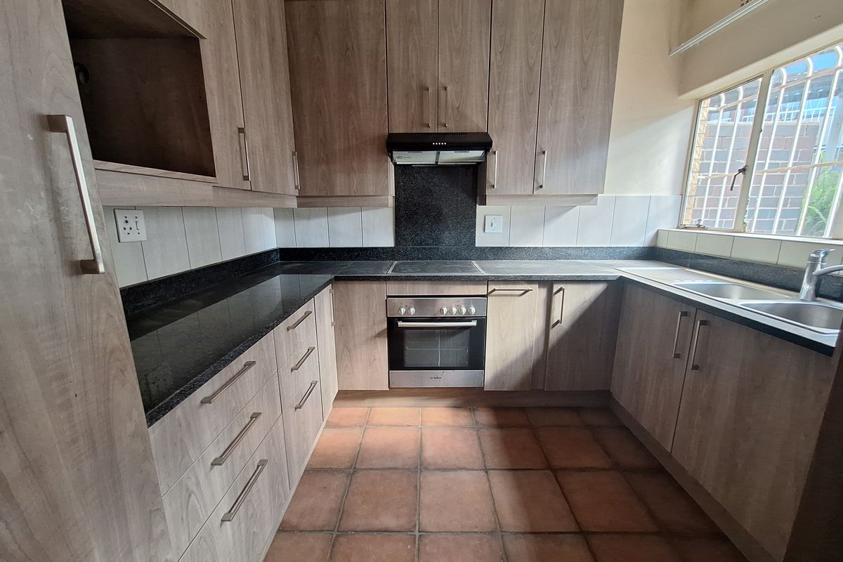 A functional kitchen featuring wood-look laminate cabinetry, granite countertops, built-in oven, electric hob, and a double bowl stainless steel sink.