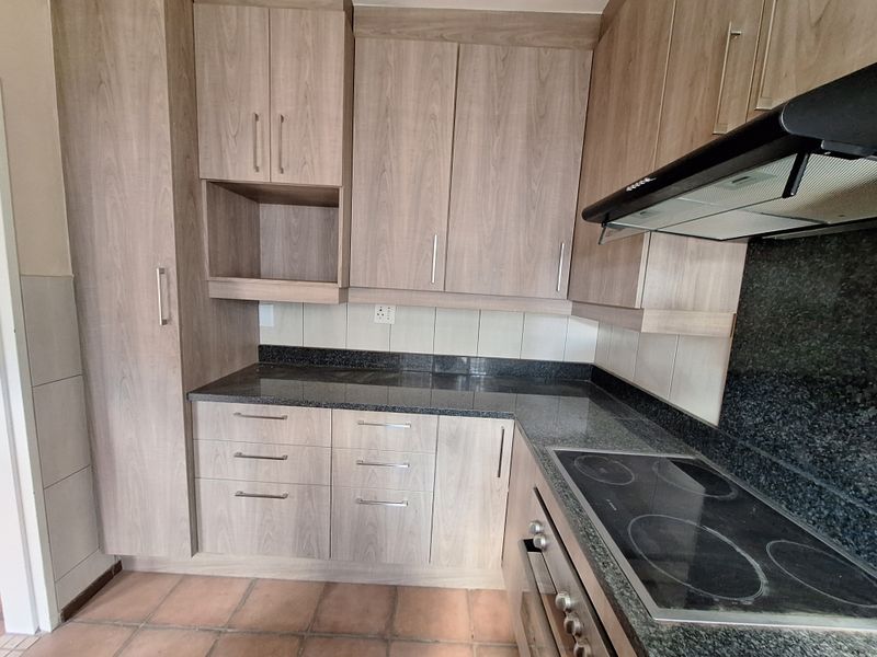 A functional kitchen featuring wood-look laminate cabinetry, granite countertops, a built-in oven, electric hob, and extractor fan with terracotta floor tiling.