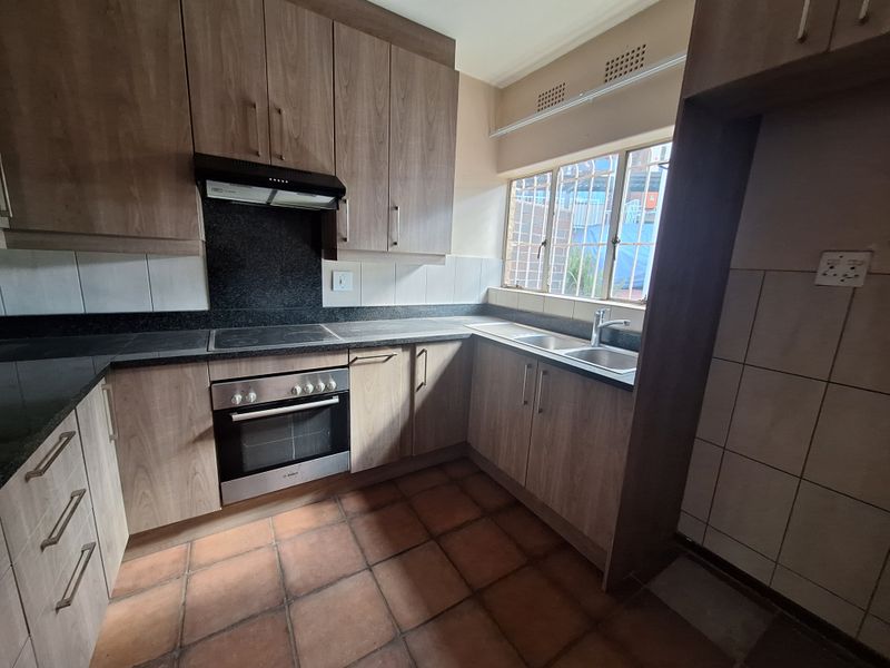 A functional kitchen featuring wood-look cabinetry, dark laminate countertops, a built-in oven with hob, and tiled flooring with security bars on the window.