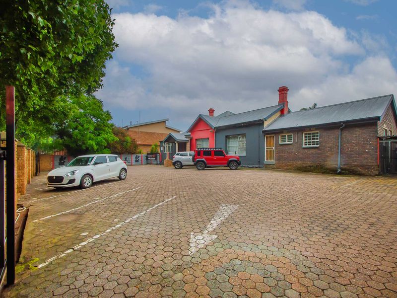 Front exterior view of the property featuring a large paved driveway, brick and painted facade, and metal roofing.