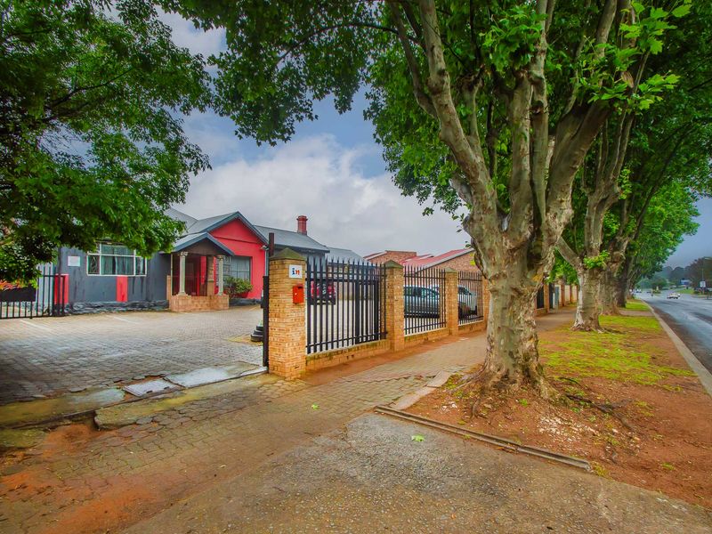 Front exterior view of the property featuring a paved driveway, secure wrought iron fencing, and brick pillars along the street frontage.