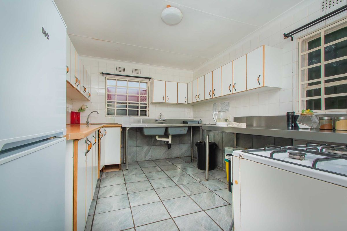 Functional kitchen featuring tiled flooring, ample built-in cabinetry, stainless steel double sink, and a gas hob with tiled splashback.