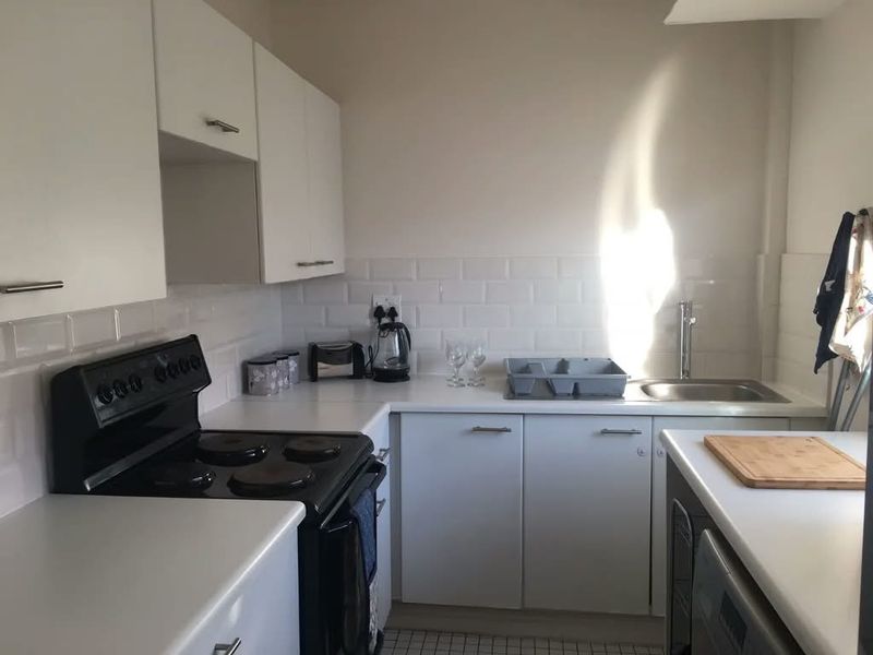 A clean and functional kitchen featuring white cabinetry, a subway tile backsplash, stainless steel sink, and a freestanding electric stove.