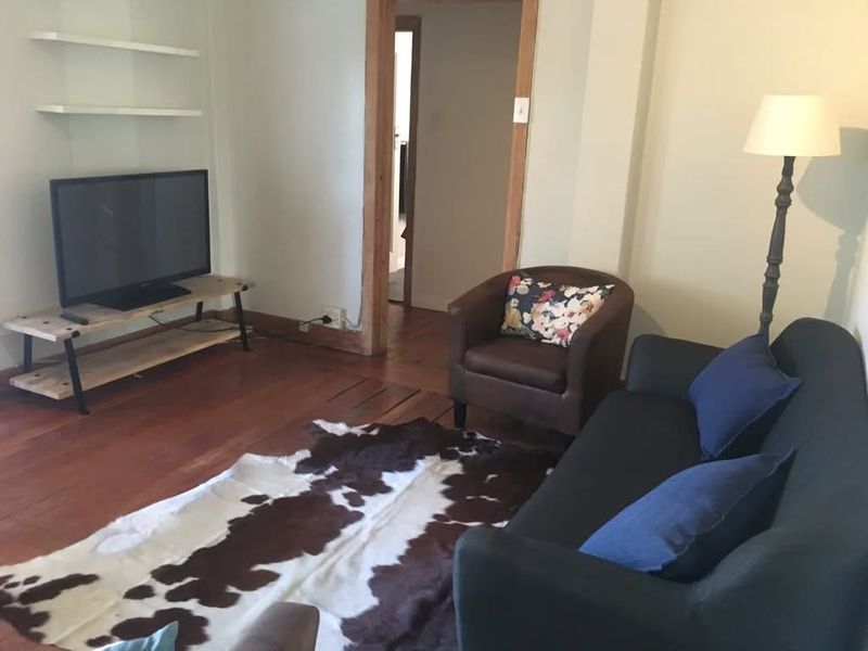 A living room featuring hardwood flooring, built-in wall shelving, and a wooden door frame leading to an adjacent space.
