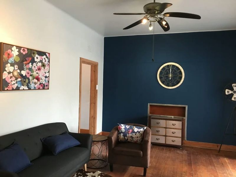 A living room featuring dark blue accent wall, hardwood flooring, and a ceiling fan, with a recessed wall niche.