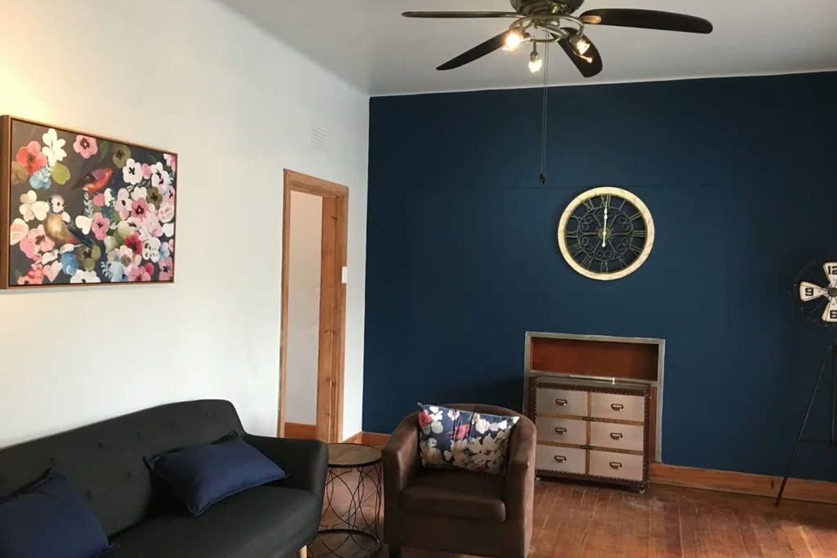 A living room featuring dark blue accent wall, hardwood flooring, and a ceiling fan, with a recessed wall niche.