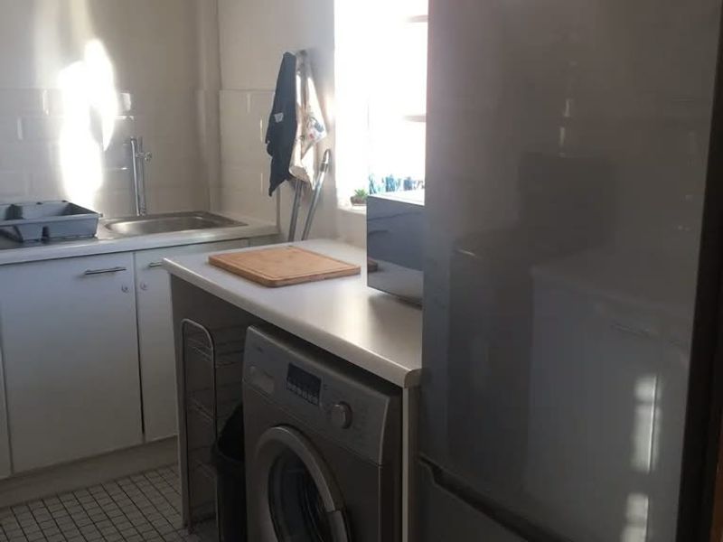 A functional kitchen area featuring tiled flooring, built-in cabinetry, a stainless steel sink, and dedicated space for laundry appliances.