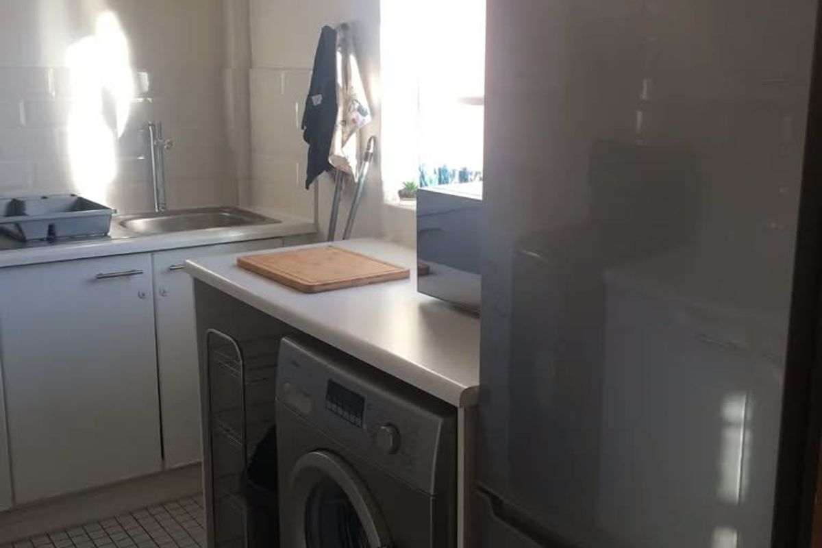 A functional kitchen area featuring tiled flooring, built-in cabinetry, a stainless steel sink, and dedicated space for laundry appliances.