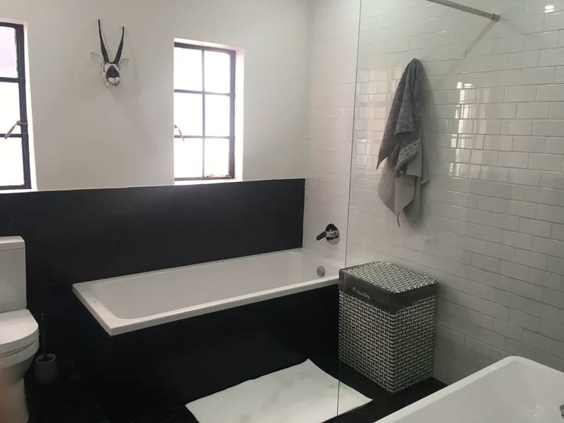 A modern bathroom featuring a bathtub, glass shower screen, subway tile wall finishes, and casement windows.