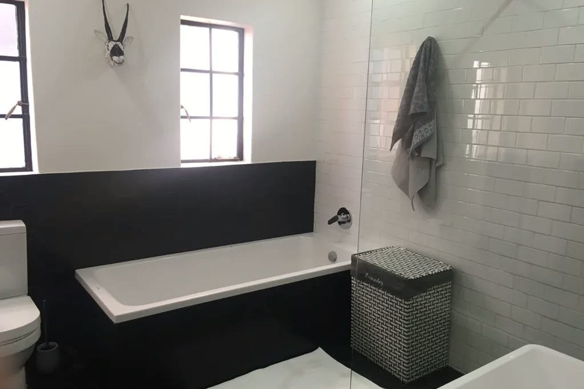 A modern bathroom featuring a bathtub, glass shower screen, subway tile wall finishes, and casement windows.