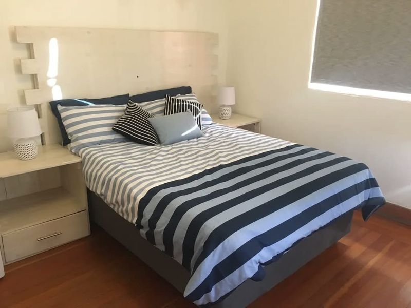 A bedroom featuring timber flooring and a roller blind, providing a functional and neutral space.