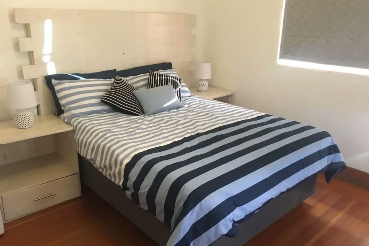 A bedroom featuring timber flooring and a roller blind, providing a functional and neutral space.